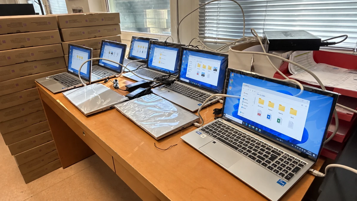 Un lot d’ordinateurs portables raccordés sur une table, avec leurs cartons à côté.