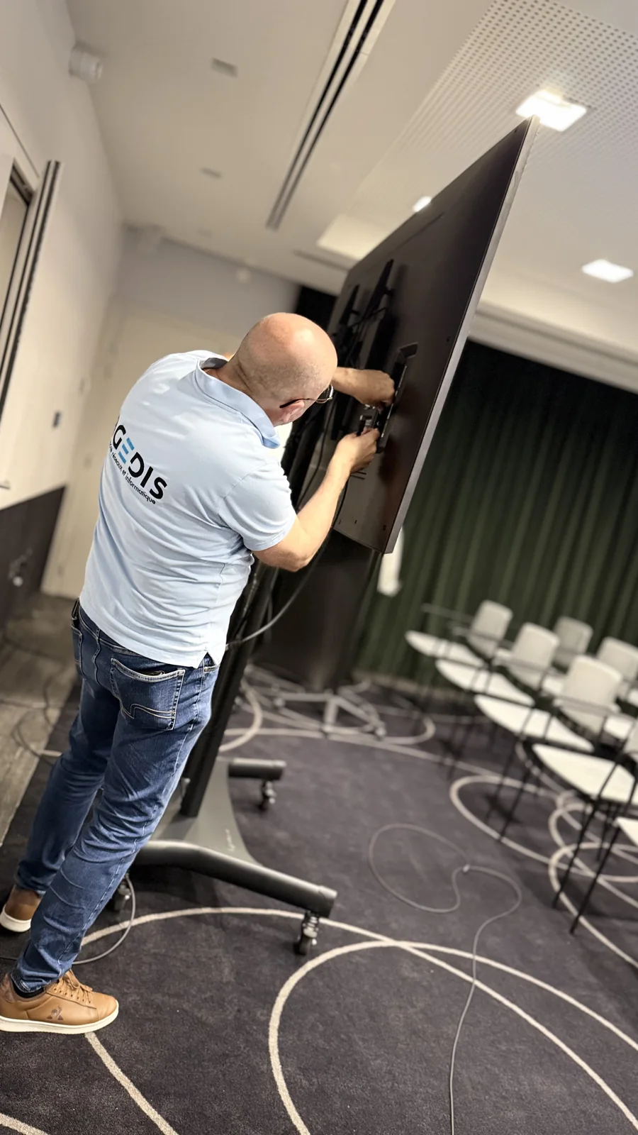 Raccordement d’un écran sur pied avant son utilisation dans une salle. Photographie d’archives de l’équipe.